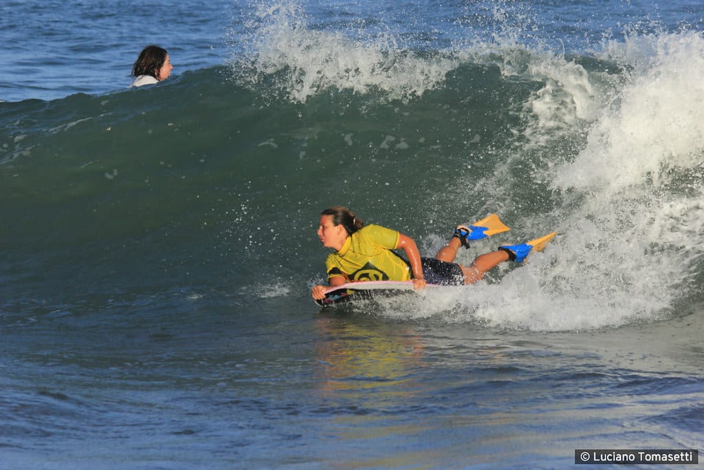 Frau die auf einem Bodyboard eine Welle surft und Bodyboard Flossen trägt