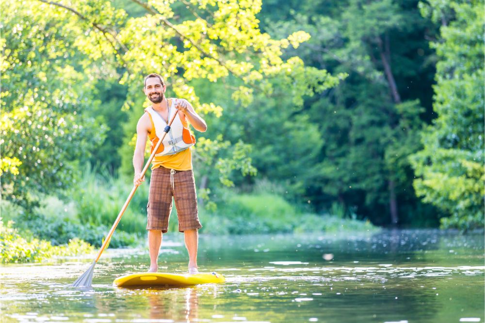 man with life jacket paddling on his paddleboard, man wearing a PFD on his paddleboard