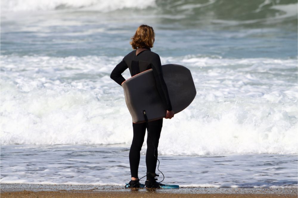 man holding a body board watching the waves