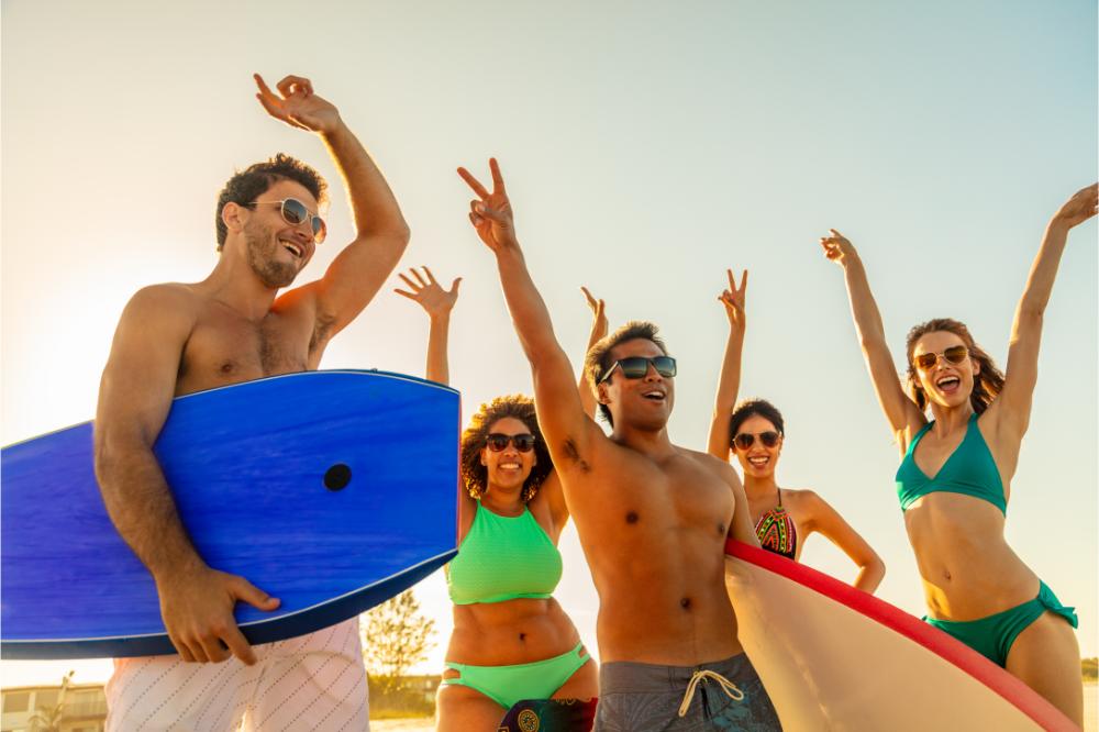 Beach celebrations for happy young friends in swimwear holding body boards on a beach.