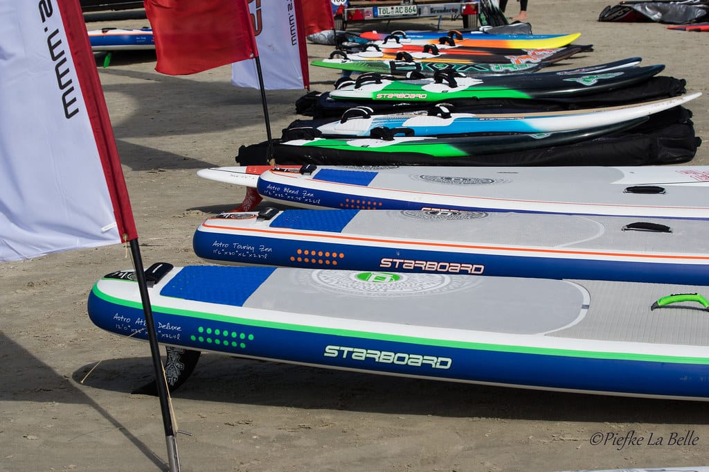 A photo of several air paddle boards across the beach in several different colours