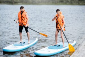 Couple in life vests learning to row on the stand up paddleboard on the lake