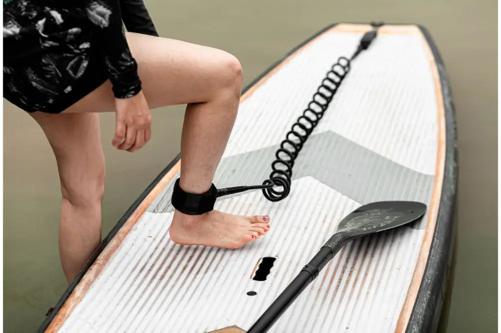 Surfboard und Paddelboard mit einer SUP Leash welche am Fussgelenk getragen wird. Bild das zeigt, wie man eine SUP Leash richtig trägt.