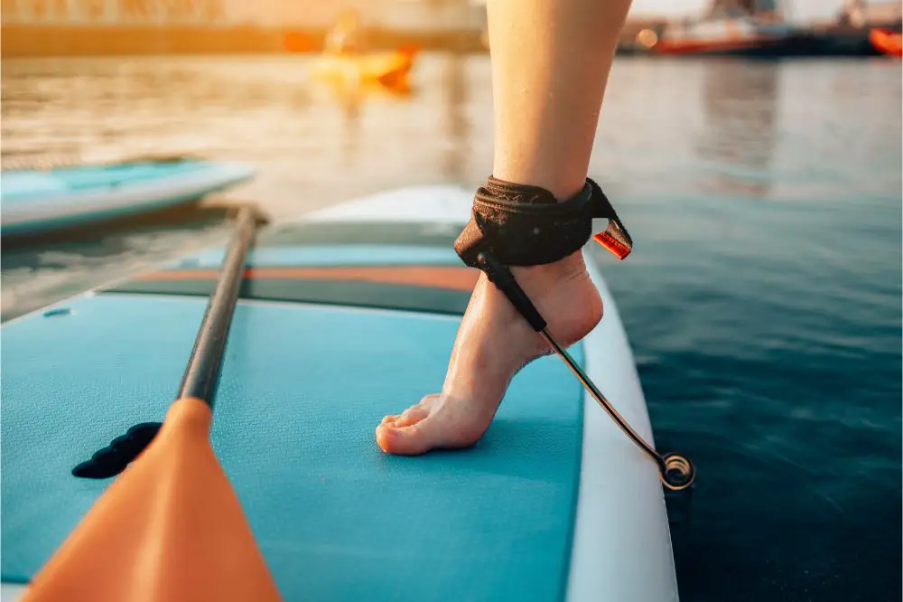 Close up of female legs standing on blue yellow color SUP stand up paddle board. How to attach paddle board leash