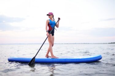 attractive young girl with SUP board on the background of the sea and sunset