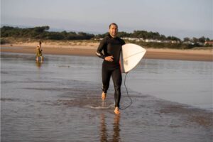 Surfer, Mann mit Surfbrett der läuft und ein UV Shirt oder ein Rash Guard trägt