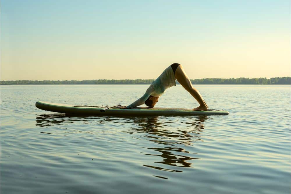 Female practicing yoga on a SUP board, Woman doing the Downward Facing Dog Yoga Pose on a SUP Board