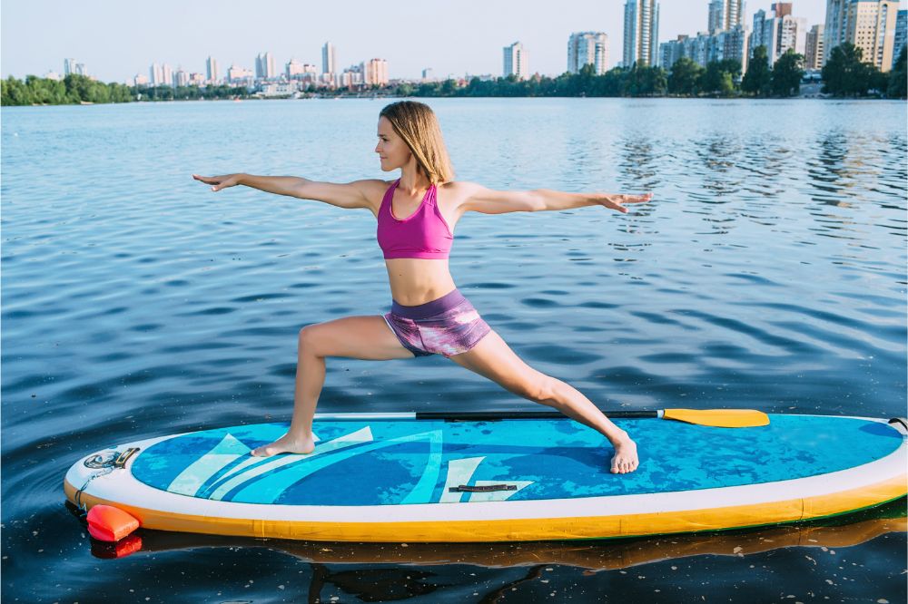 Young woman doing yoga pose on paddle board, woman doing the Warrior 1 Yoga Pose on a Stand Up Paddle Board