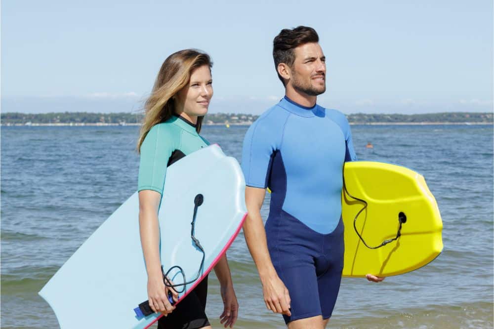 two surfers walking with bodyboards along the beach