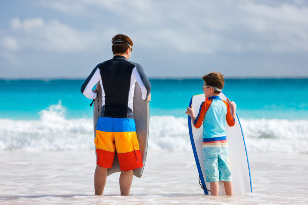 Picture showing a man and a boy with bodyboards. The Bodyboard of the boy is a little too big. Picture is used in an article which answers the question can a bodyboard be too big?