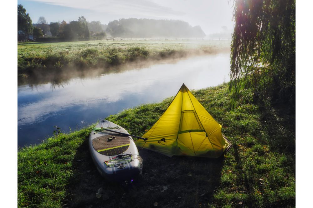 SUP (Stand up paddling) board next to a small tent at river