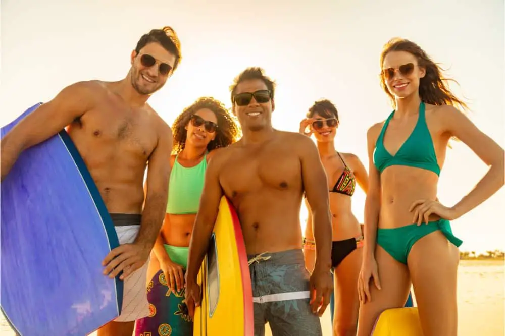 Smiling friends carrying bodyboards having fun on beach