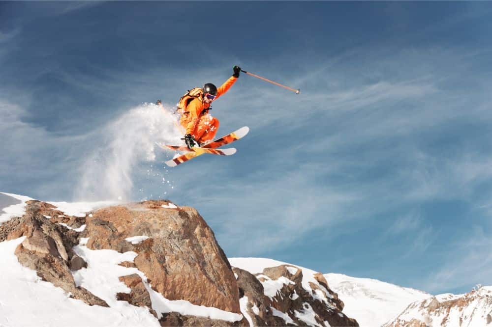 An athlete skier is jumping from high rock high in the mountains using powder skis