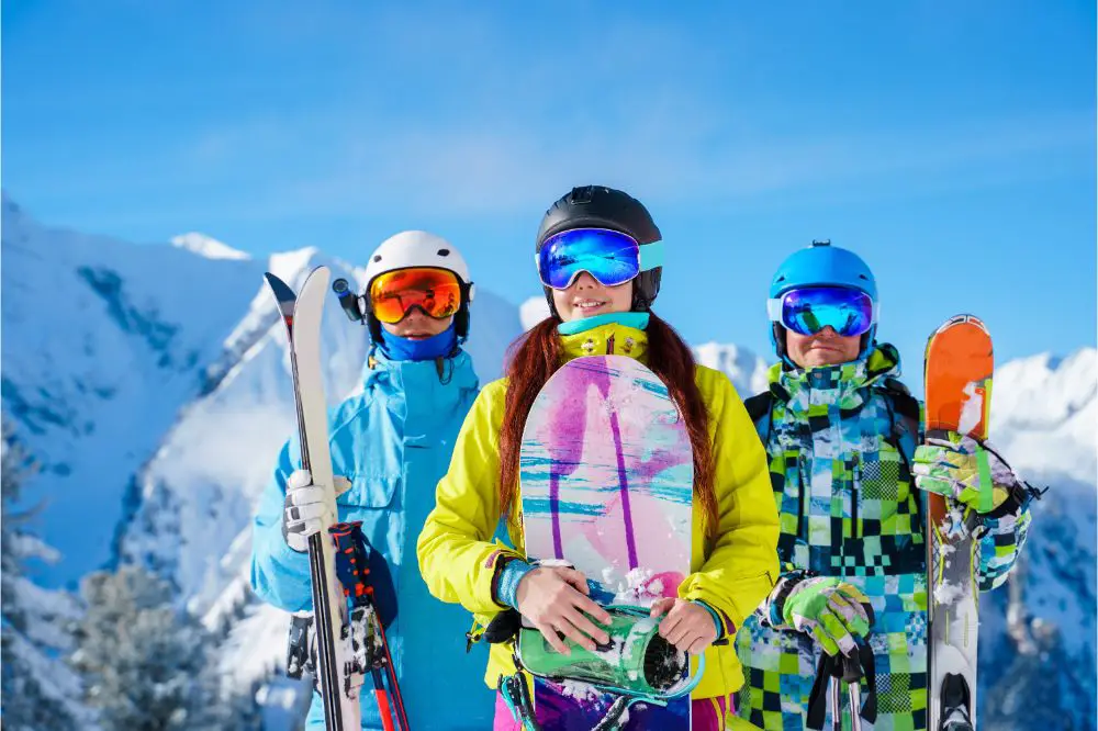Two men and woman with snowboard and skis standing on snow resort