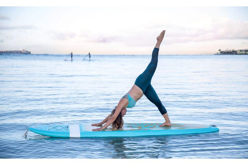 Athletic young woman in SUP Yoga practice side bend leg lift Pose. woman doing fitness on a Stand Up Paddle Board