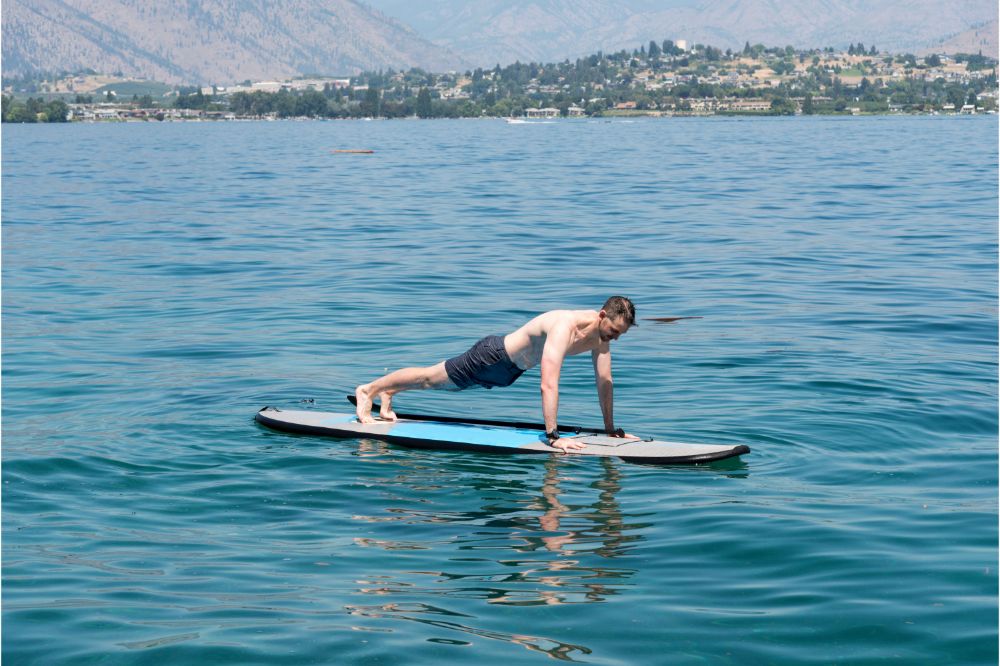 Man doing push-ups while floating on paddle board in the middle of the sea