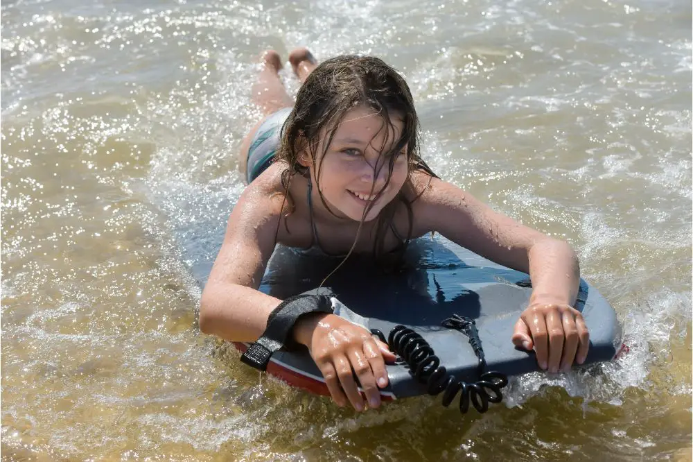 Beautiful young girl playing bodyboard in the waves in summer