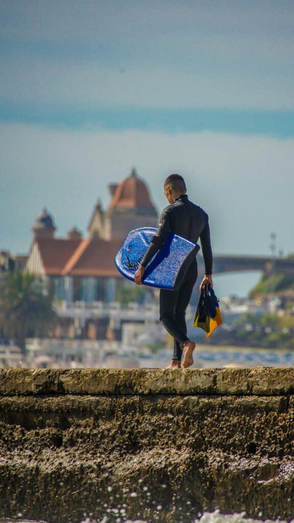 man carrying a bodyboard used in an article about how to take care of a boadyboard and how to maintain a bodyboard