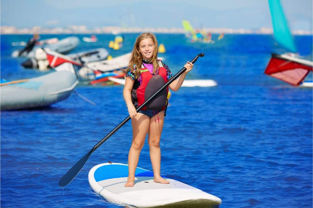 Kid paddle surf surfer girl with row in the beach, Girl on a Stand-Up Paddle Board having fun used in an article explaning how to learn Stand-Up Paddleboarding for Kids