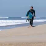 Bodyboarder walking on the beach in a wet suit holding a bodyboard and fins