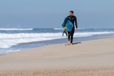 Bodyboarder walking on the beach in a wet suit holding a bodyboard and fins