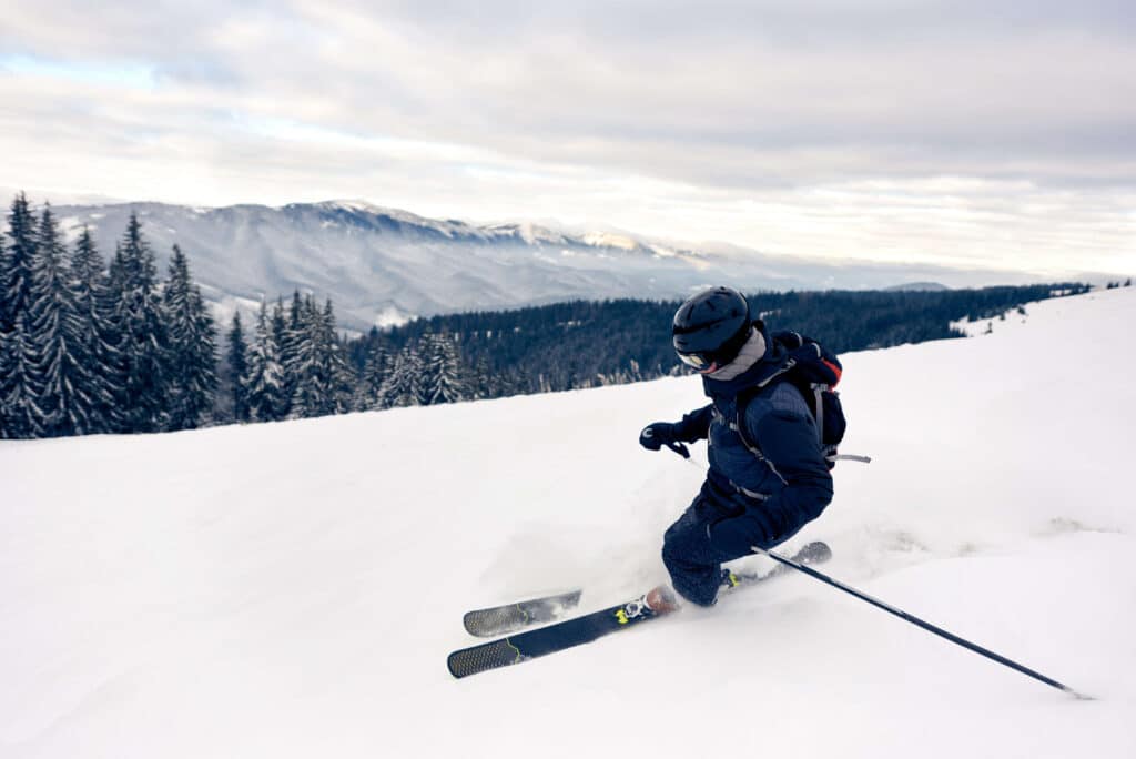 A person at the top of a snow-covered mountain demonstrating the 'Carving' skiing technique to control their speed down the slope.