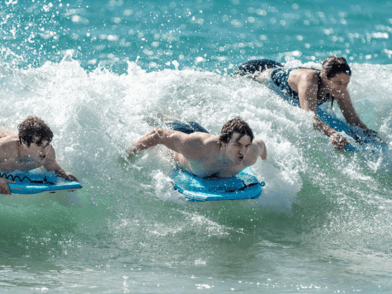 A group of friends riding waves into shore on their paddleboards, all smiling after spending time in the ocean