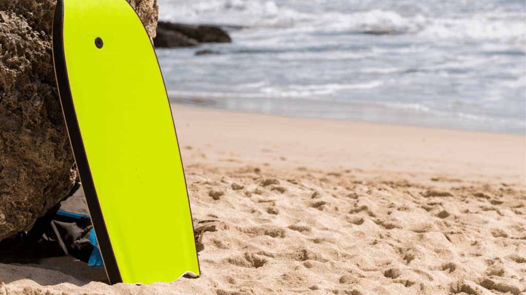 A yellow bat tail bodyboard against a rock on a sandy beach near the ocean