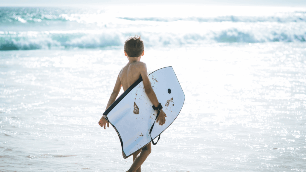 A child carrying a white crescent tail bodyboard into the ocean