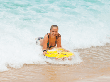 A woman on a yellow bodyboard riding a wave into shore