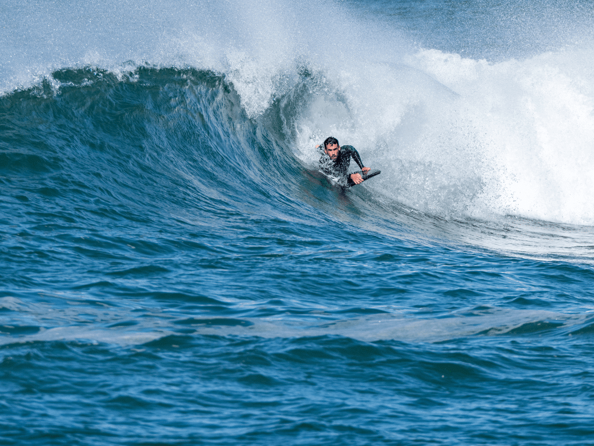 A man wearing a wetsuit riding a wave on a body board