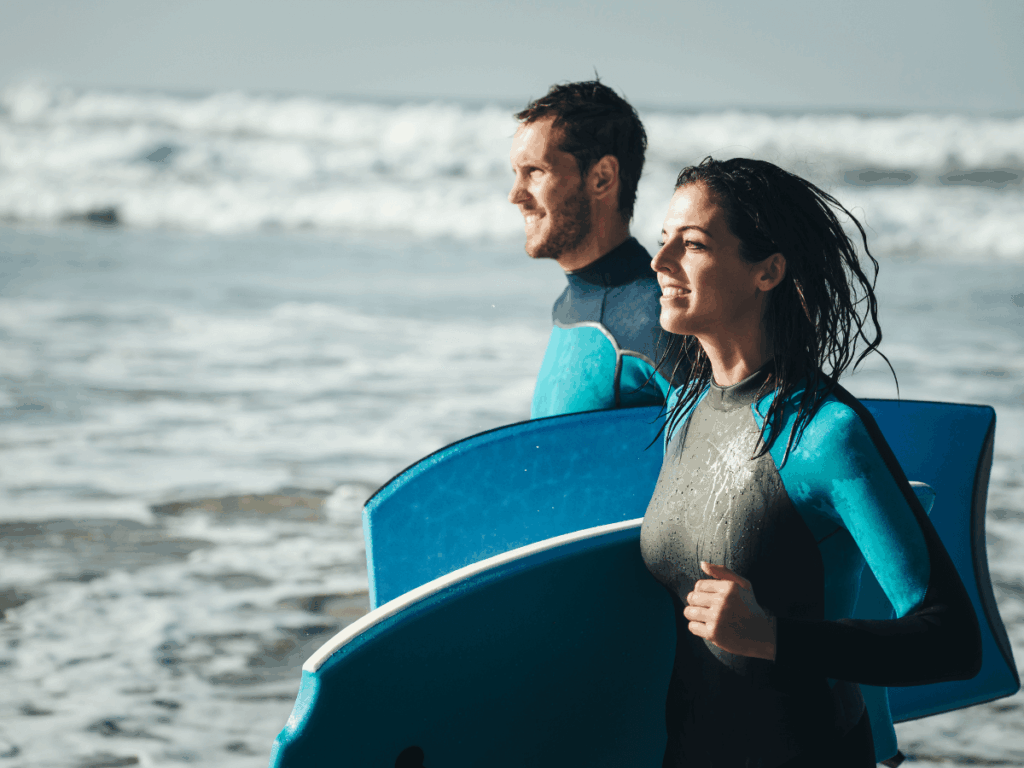 A couple walking into the sea wearing wetsuits carrying their bodyboards