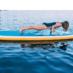 A young woman demonstrating doing a plank on her paddleboard to help strengthen her core.