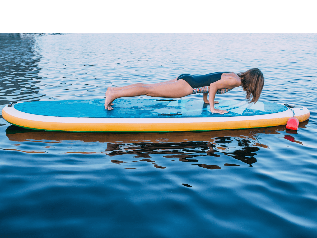 A young woman demonstrating doing a plank on her paddleboard to help strengthen her core.