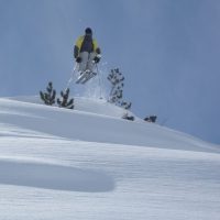 a person in a yellow jacket skiing jumping off a snowy hill